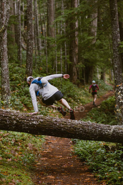 Un uomo salta sopra l'albero abbattuto mentre il sentiero corre con un amico — Foto stock