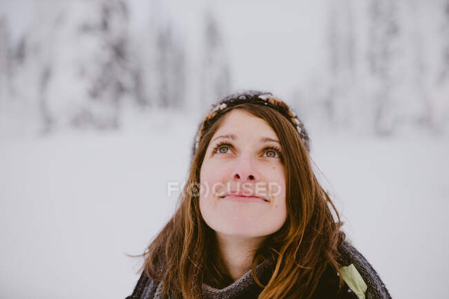 Young woman with brown hair and eyes looks up at snow covered trees — Stock Photo