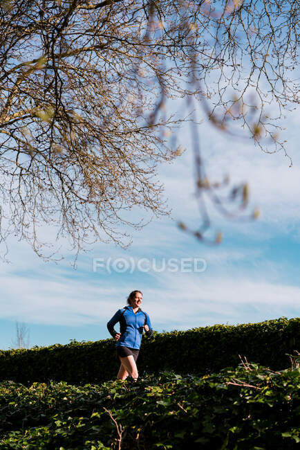 Junge Frau läuft auf gepflastertem Weg unter Bäumen und blauem Himmel — Stockfoto