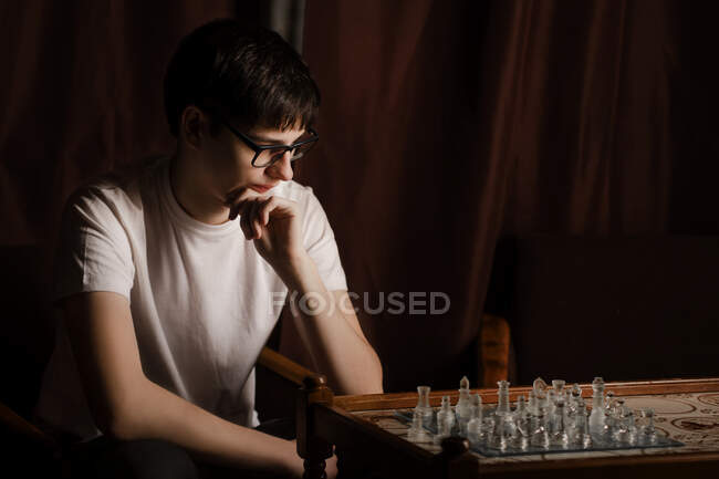 Парень в очках смотрит на шахматную доску — стоковое фото
