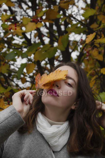 Girl holding yellow leaf near face — Stock Photo