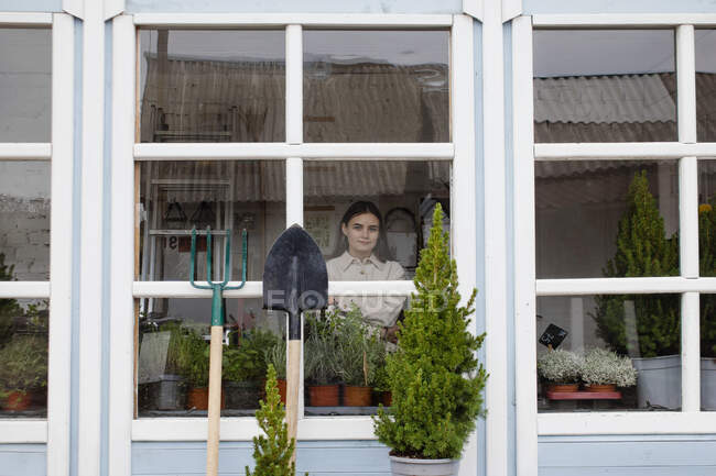 Young girl in garden workshop looking through window — Stock Photo