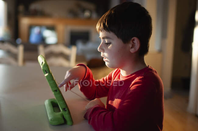 Menino 9-10 anos de idade brincando com seu tablet no balcão da cozinha — Fotografia de Stock