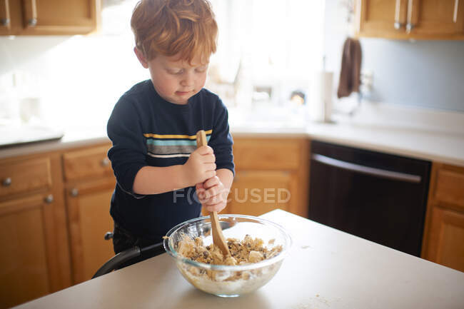 Menino 3-4 anos de idade misturando massa de biscoito no balcão da cozinha em casa — Fotografia de Stock