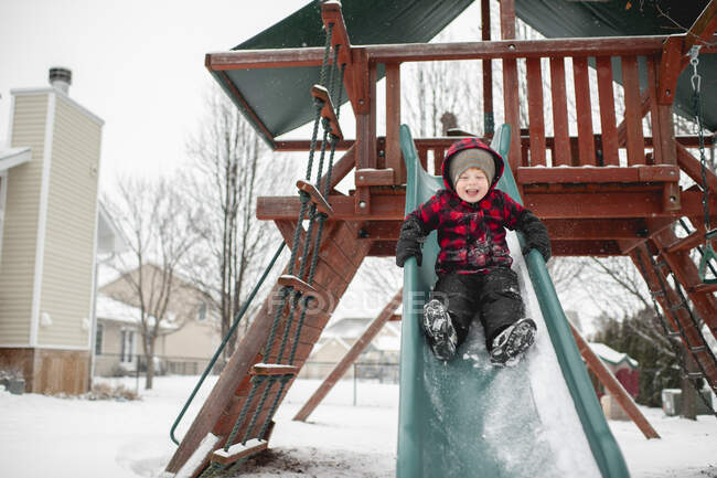 Happy boy 3-4 years old slides down slide in winter weather — Stock Photo