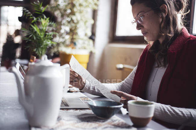 Mulher trabalha em casa escritório com papelada laptop e xícara de chá — Fotografia de Stock