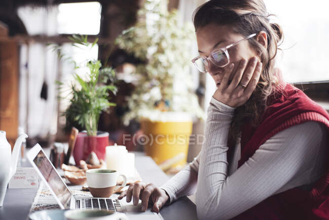 Профессиональная женщина в очках типов на компьютере в домашнем офисе с чаем — стоковое фото