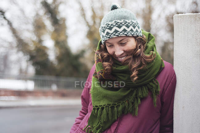 Pretty woman in beanie and scarf leans on post outside smilinn — Stock Photo