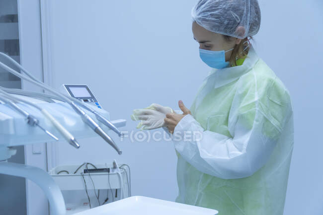 Woman dentist wearing safety equipment with mask putting glove on hand — Stock Photo
