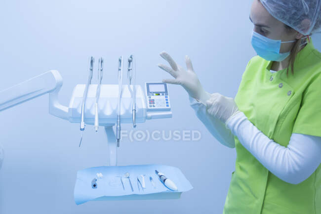 Mulher dentista com máscara colocando luvas em uma clínica odontológica — Fotografia de Stock