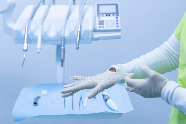 Dentista poniéndose guantes en las manos en una clínica dental - foto de stock