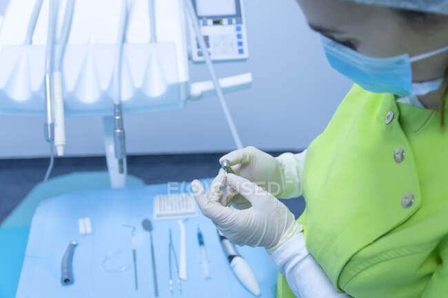 Mujer dentista con máscara y guantes preparando el taladro, clínica dental - foto de stock