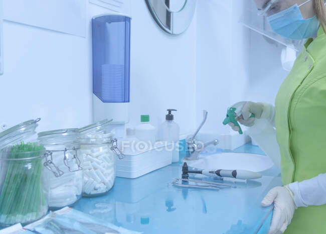 Mujer dentista con máscara y guantes desinfectando los instrumentos - foto de stock