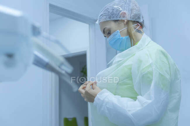 Mujer dentista poniéndose ropa protectora, clínica dental - foto de stock