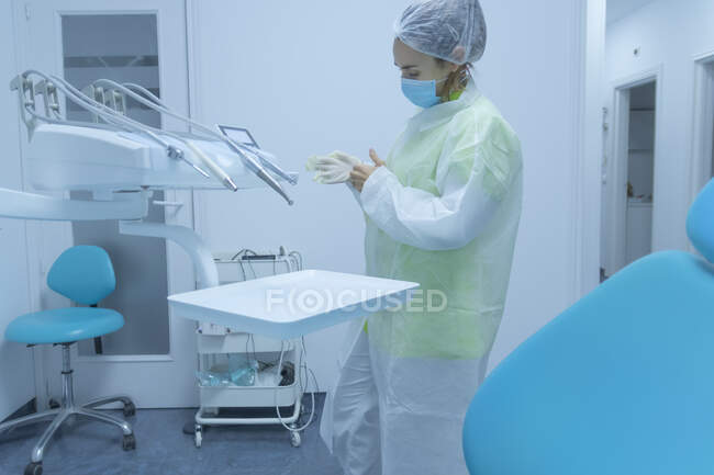 Mujer dentista en ropa protectora poniéndose guantes, clínica dental - foto de stock
