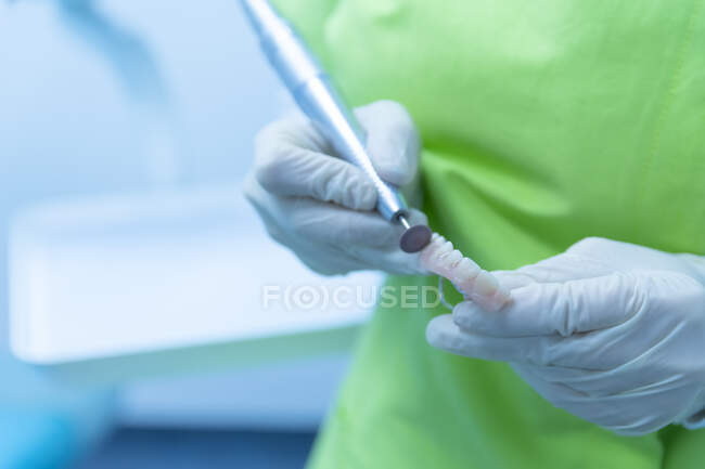 Dentist's hands in protective clothing doing denture cleaning, clinic — Stock Photo