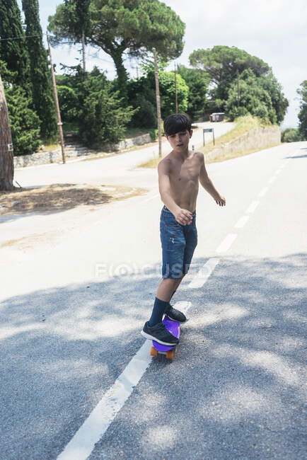 Portrait of cheerful shirtless teen skateboarding on mountain road — Stock Photo