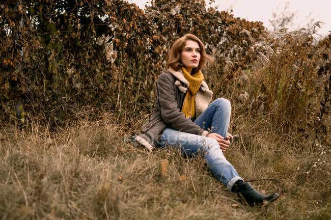 Retrato de una mujer joven con suéter sentado en la hierba - foto de stock