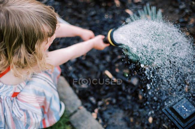 Bambina annaffiare le piante nel cortile — Foto stock