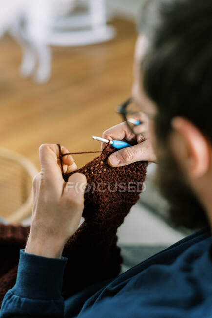 Millennial man crocheting a sleeve of a child pullover with his hands — Stock Photo