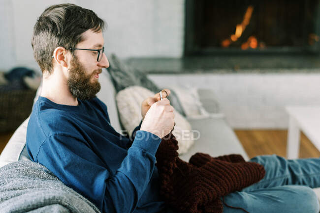 Millennial-Mann häkelt einen Pullover für seinen Sohn am Kamin — Stockfoto