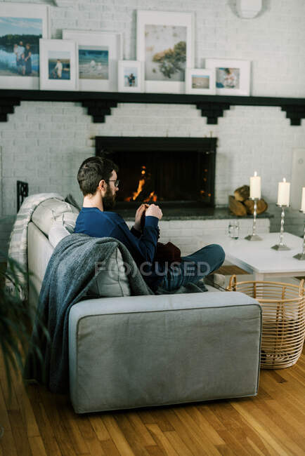 Тысячелетний мужчина вяжет крючком в своей гостиной у теплого и уютного огня — стоковое фото