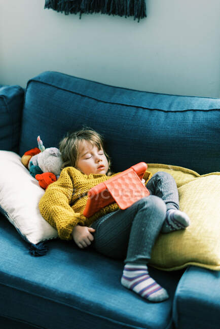 Little toddler girl in primary colors sleeping on sofa with tablet — Stock Photo