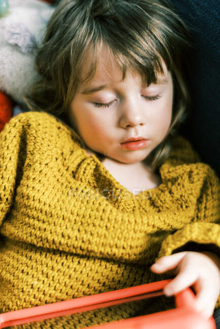 Маленька дівчинка в первинних кольорах спить на дивані з планшетом — стокове фото
