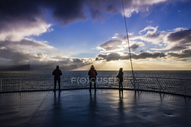 Trois personnes profitent du coucher de soleil sur le pont du bateau qui part pour l'Islande — Photo de stock