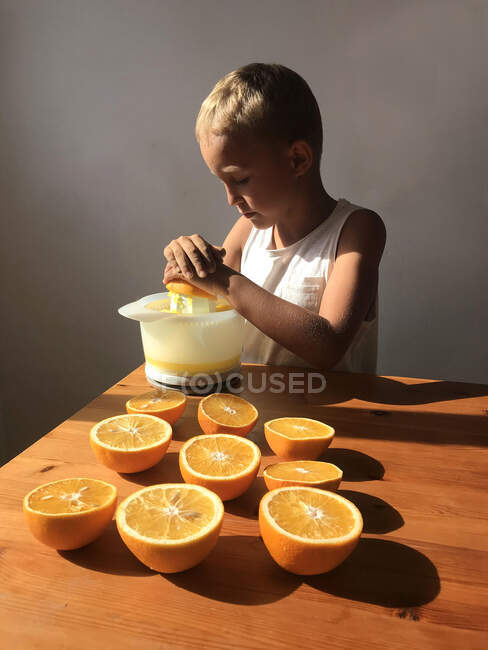 O ajudante da pequena mãe. Menino faz um suco de laranja na cozinha. — Fotografia de Stock