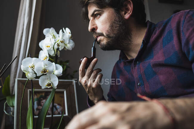 Un uomo sulla quarantina guarda fuori da una finestra fumando una pipa. Concetto di bein — Foto stock