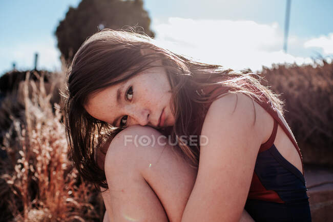 Adolescente chica en un traje de baño sentado fuera en un día soleado - foto de stock