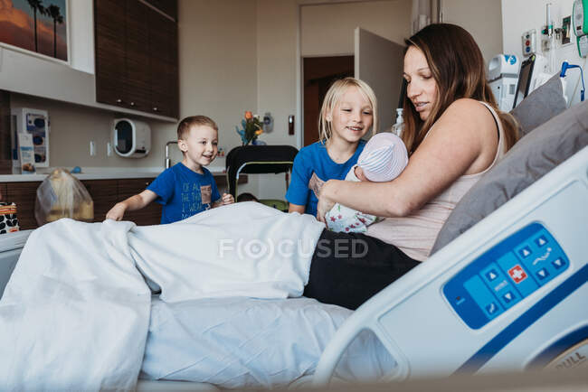 Hermanos jóvenes conociendo al bebé recién nacido por primera vez en el hospital - foto de stock