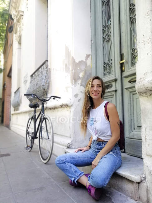 Mujer feliz mirando hacia otro lado mientras está sentada en bicicleta fuera del edificio - foto de stock