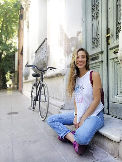 Happy woman while sitting by bicycle outside building — Stock Photo