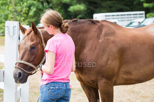 Junges Mädchen steht mit braunem Pferd vor einem Reitturnier — Stockfoto