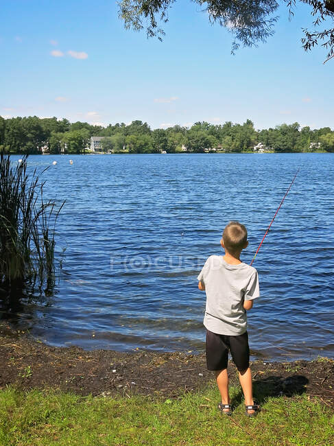 Jeune garçon avec la canne à pêche à un étang en été bobinage dans son poisson — Photo de stock