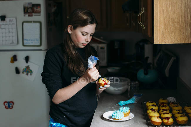 Adolescente menina decorando cupcakes na cozinha — Fotografia de Stock