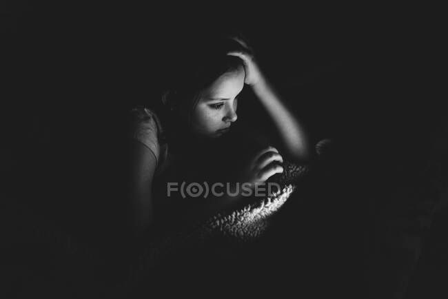 Menina usando um tablet em um quarto escuro — Fotografia de Stock