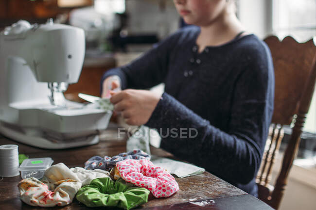 Ragazza seduta al tavolo della cucina che fa cravatte per capelli sulla macchina da cucire — Foto stock