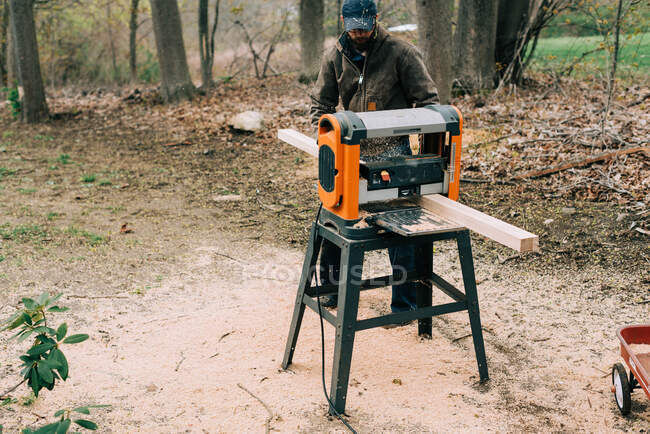 Millennial man planing white oak wood with a planer outside in spring — Stock Photo