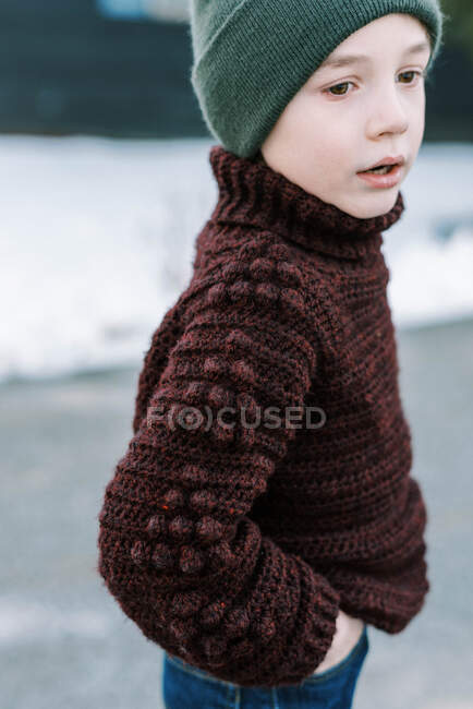Little boy with hat in a homemade sweater standing outside in snow — Stock Photo