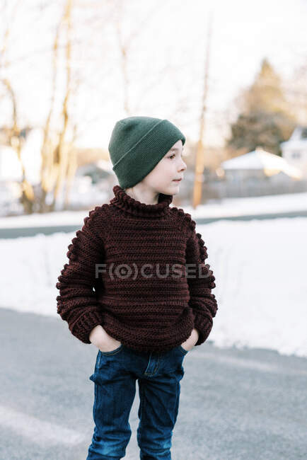 Petit garçon avec chapeau dans un pull fait maison debout dehors dans la neige — Photo de stock