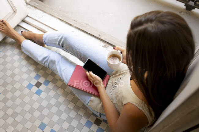 Giovane donna seduta al piano con telefono cellulare e caffè — Foto stock