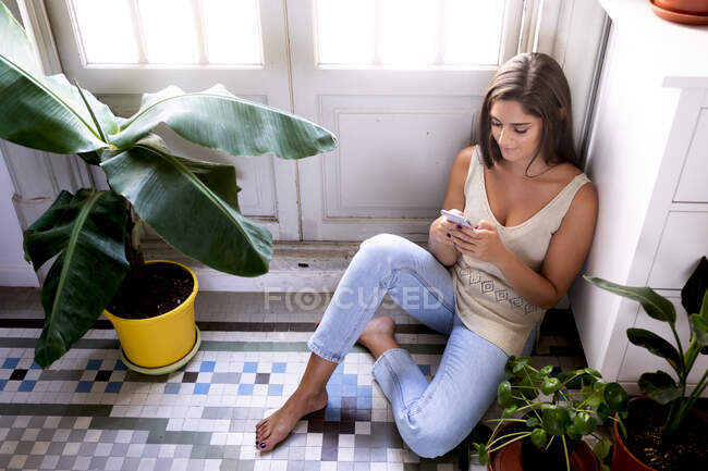 Молода жінка сидить на підлозі і дивиться на смартфон — стокове фото