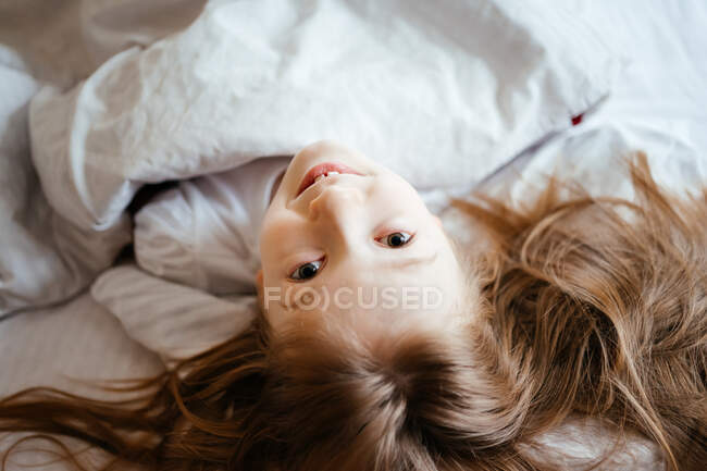 Девушка смотрит в камеру, лежа на белой кровати — стоковое фото