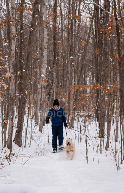 Teen boy snowshoeing with dog in the woods on a snowy winter day. — Stock Photo