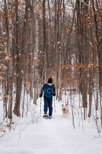 Teen boy snowshoeing with dog in the woods on a snowy winter day. — Stock Photo