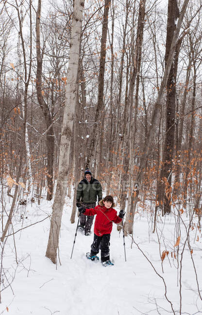 Giovane ragazzo ciaspolata con il padre nei boschi in una giornata invernale innevata. — Foto stock