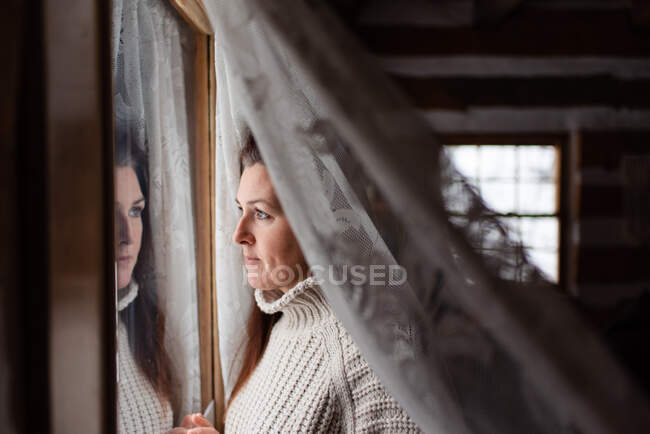 Belle femme regardant par la fenêtre derrière un curatin de dentelle. — Photo de stock